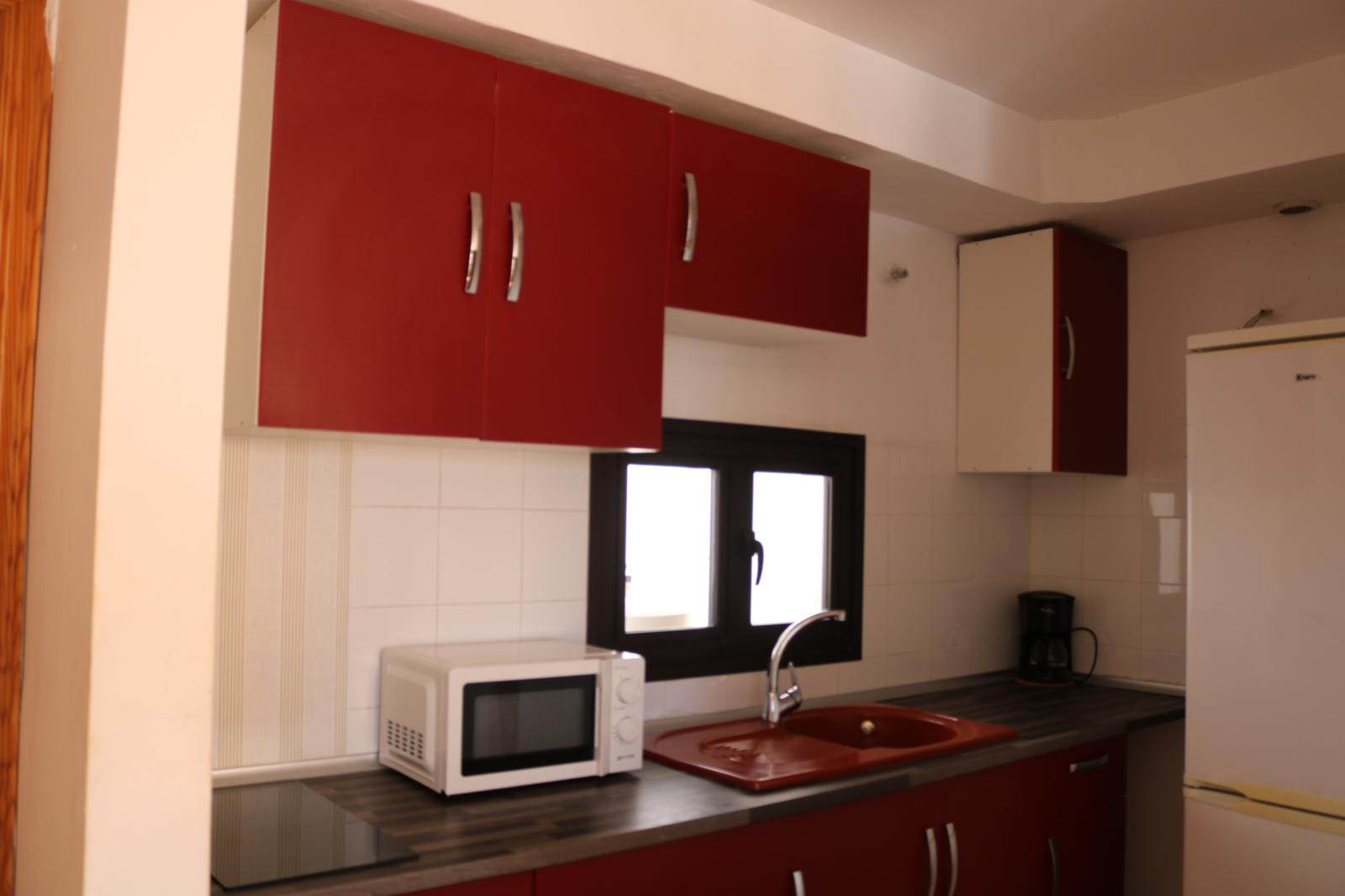 Cocina completa del apartamento con mobiliario rojo, microondas y cafetera