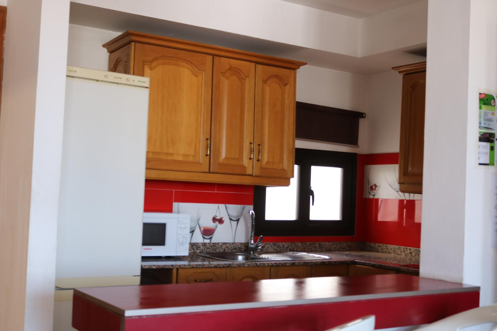 Cocina abierta del apartamento con mobiliario de madera y detalles rojos