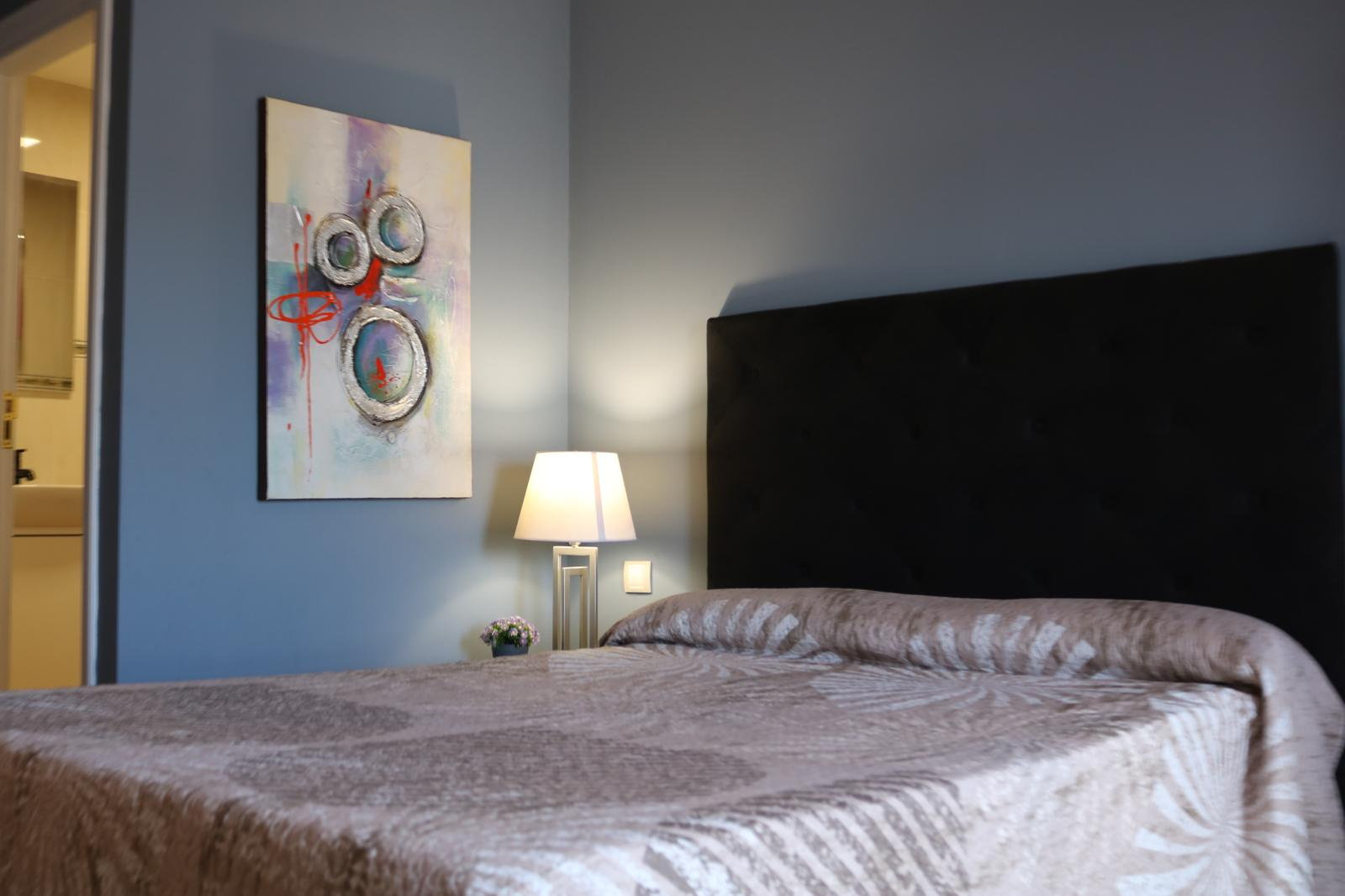 Dormitorio del Estudio con cama doble grande, cabecero oscuro y lámpara de lectura